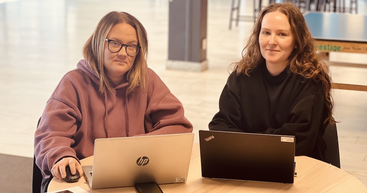 två unga kvinnor med laptopdatorer tittar mot kameran