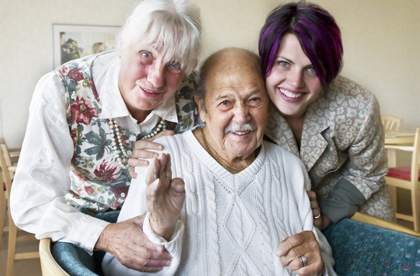 En äldre man sitter i mitten med två kvinnor på vardera sida om honom.