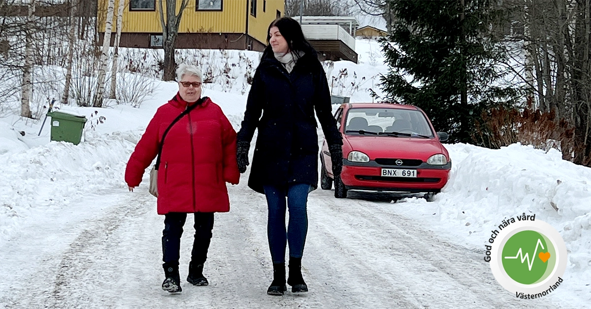 Hillevi har röd jacka och går till vänster, Sofia har svart jacka och går till höger. Det är vinter. Bakom dem står en röd personbil.