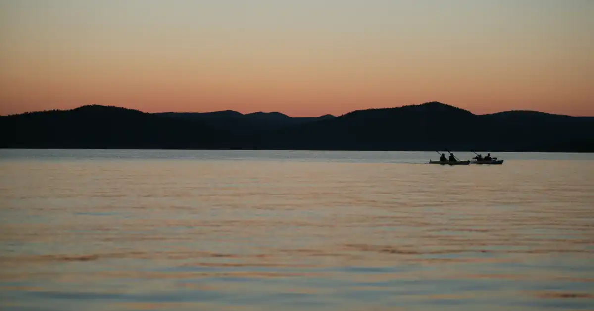 solnedgång bakom berg, i förgrunden hav och fyra personer som paddlar i två dubbelkajaker