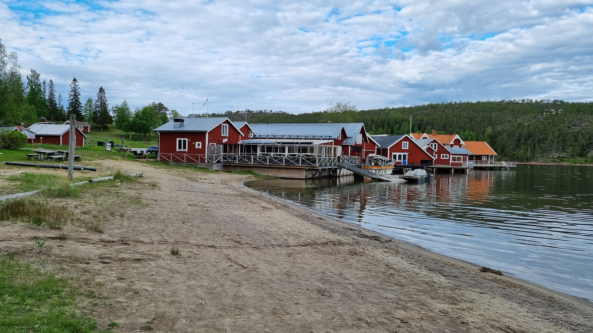 En tom badstrand vid havet i Norrfällsviken och i bakgrunden ser man ett rött hus som är en restaurang vid namn Fiskarfänget.