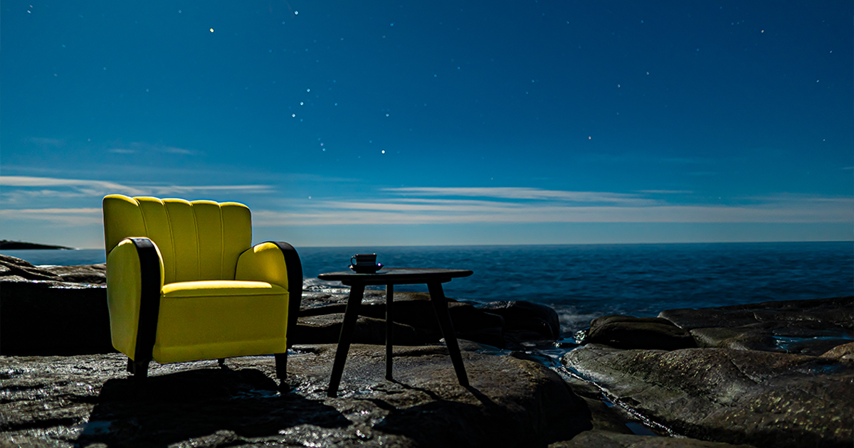En fåtölj och ett soffbord som står vid havet under en stjärnklar himmel.