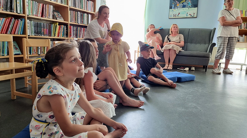 Ukrainska barn sitter på kuddar på golvet och tittar på en film.