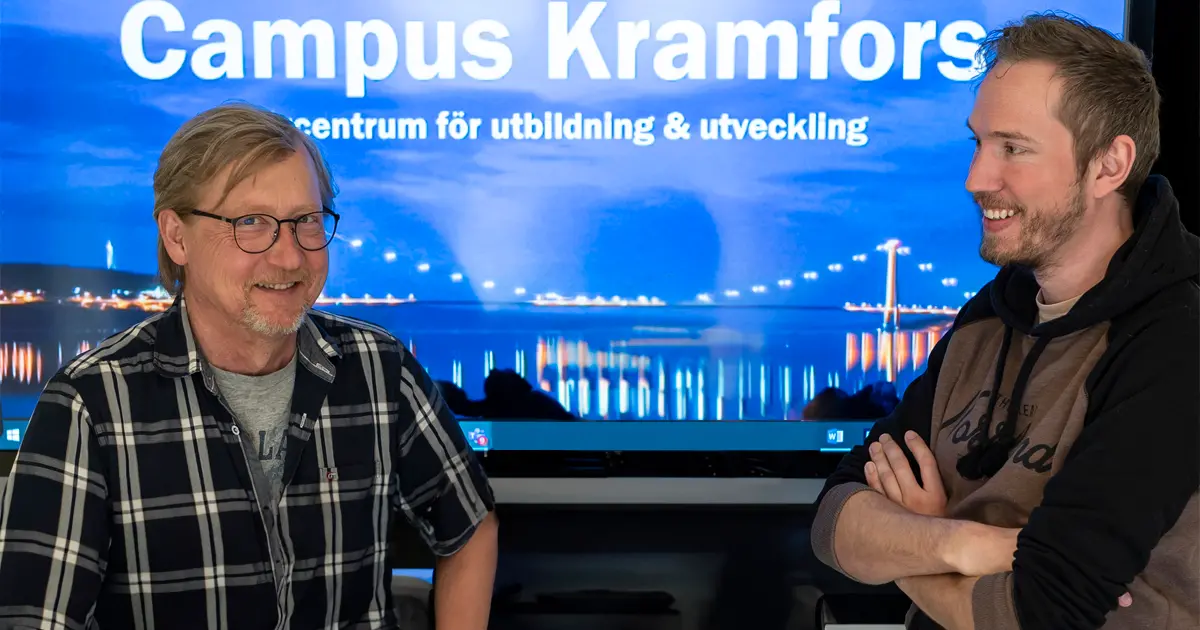 Göran Mellander, verksamhetsutvecklare och Carl Sundström, administratör på Campus Kramfors ser glada ut och står framför en skärm som visar Campus Kramfors logotyp.