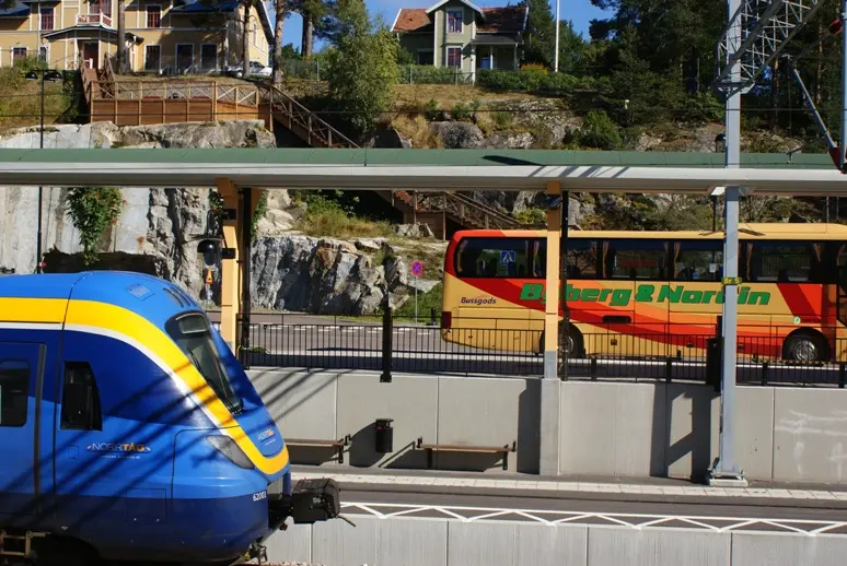 Bilden visar Kramfors Resecentrum med ett tåg på perrongen och en buss i bakgrunden.