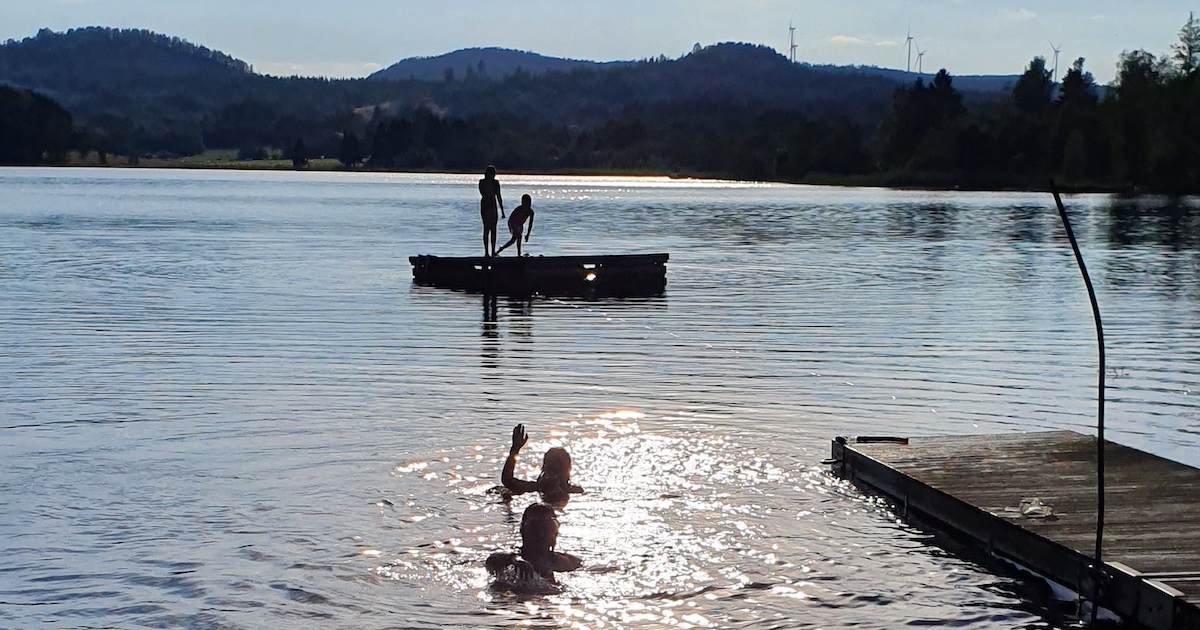 Barn och ungdomar som badar från bryggor, i sjö, i sommarsol