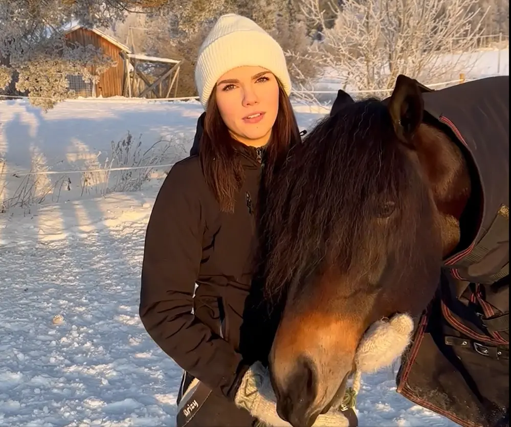 En ung kvinna står bredvid sin häst, vinterlandskap.