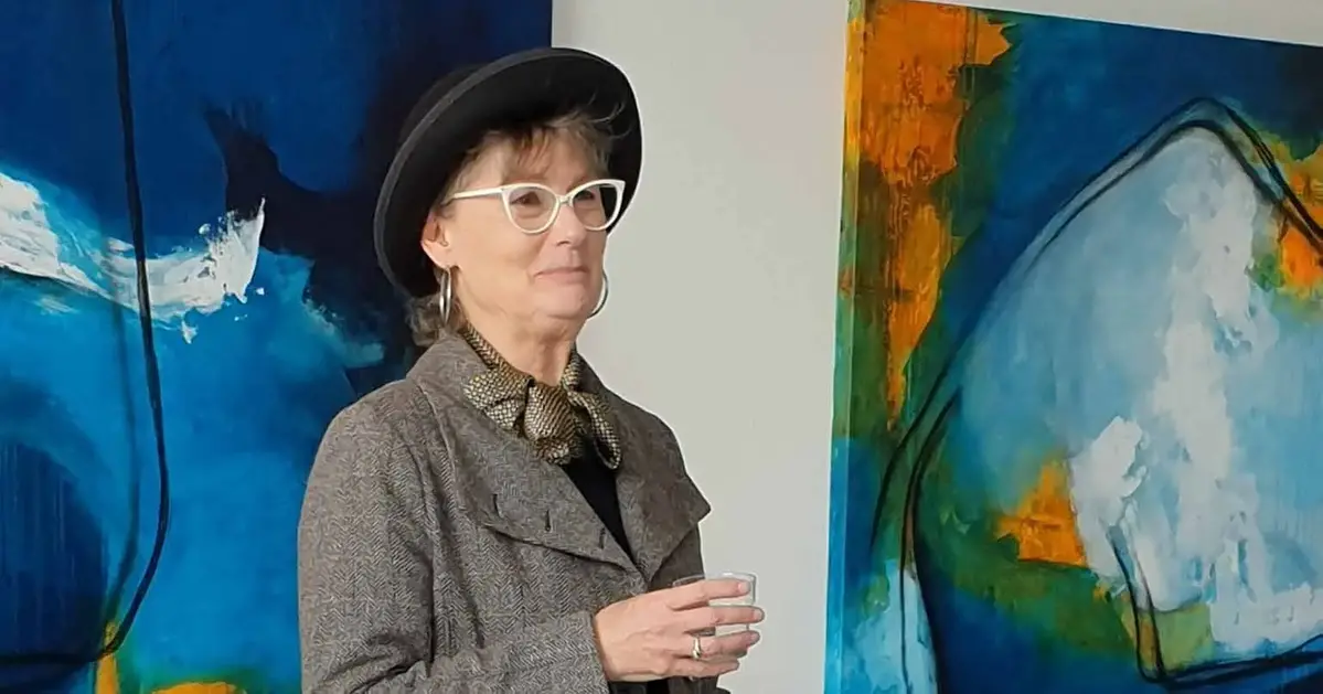  Annika Johansson, ordförande för Kramfors konstförening, står framför två färgstarka målningar i Kramfors konsthall.