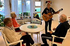 Sylvia Sandin sjunger för tre äldre personer som sitter vid ett runt bord.